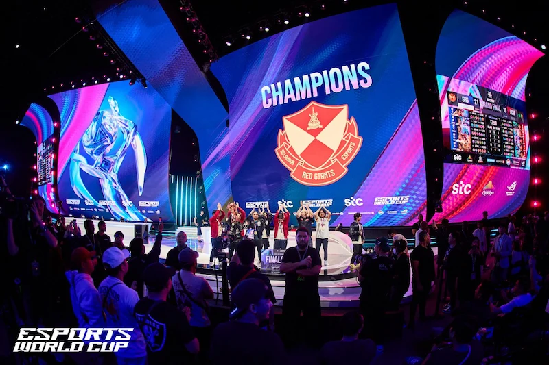 Vinnarna av Esports World Cup 2024 firar på scenen framför en stor LED-skärm med laglogotyp och texten "Champions".