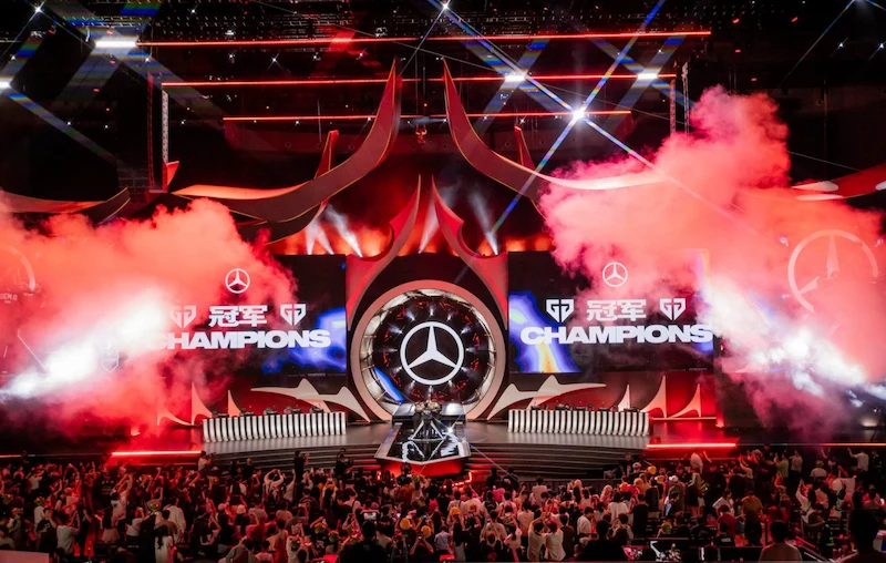 Segrarna kröns under Mid-Season Invitational 2024 med röd rök, Mercedes-logga och texten "Champions" på storbildsskärmen.