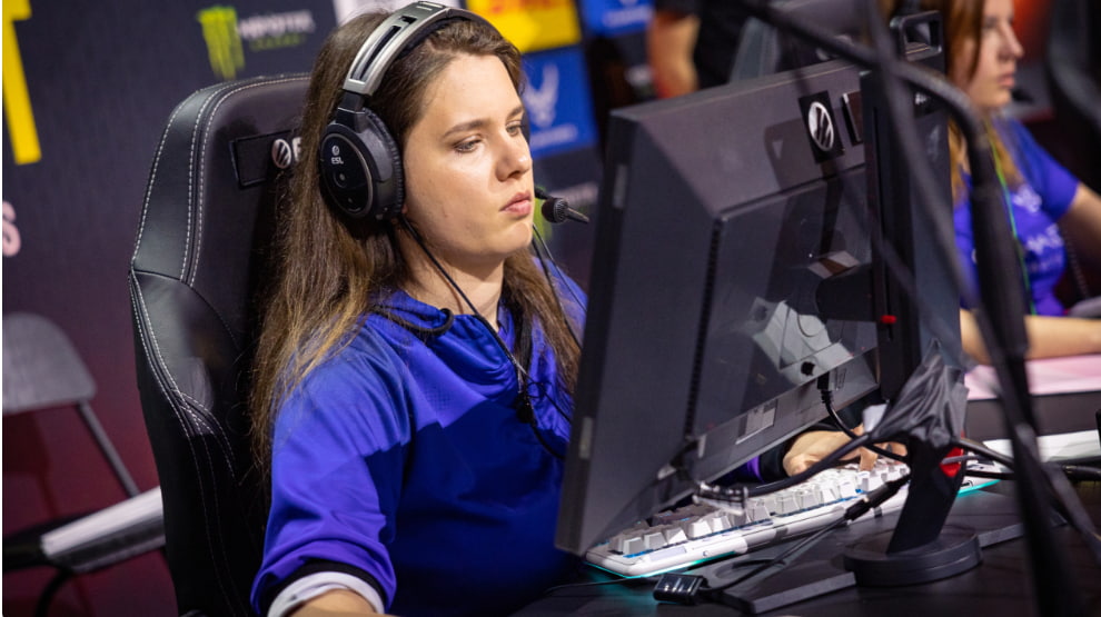 Självsäker ung kvinna med headset spelar datorspel framför en skärm, koncentrerad på spelet.