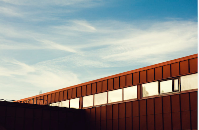 Röd byggnad med fönster under blå himmel, Tumba Gymnasium, en modern skolbyggnad i soligt väder