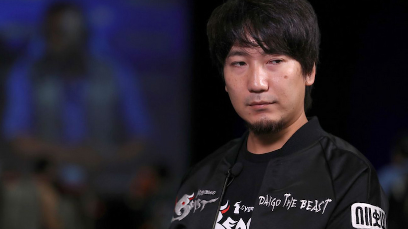 Person i svart jacka med texten "Daigo The Beast" på en scen, troligen vid ett e-sportevent.