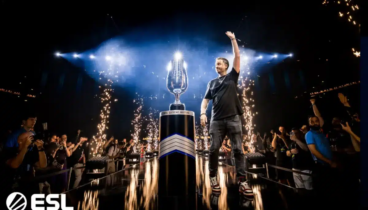En glad vinnare vinkar bredvid den stora ESL-trofén på en upplyst scen med fyrverkerier och publik runt om.