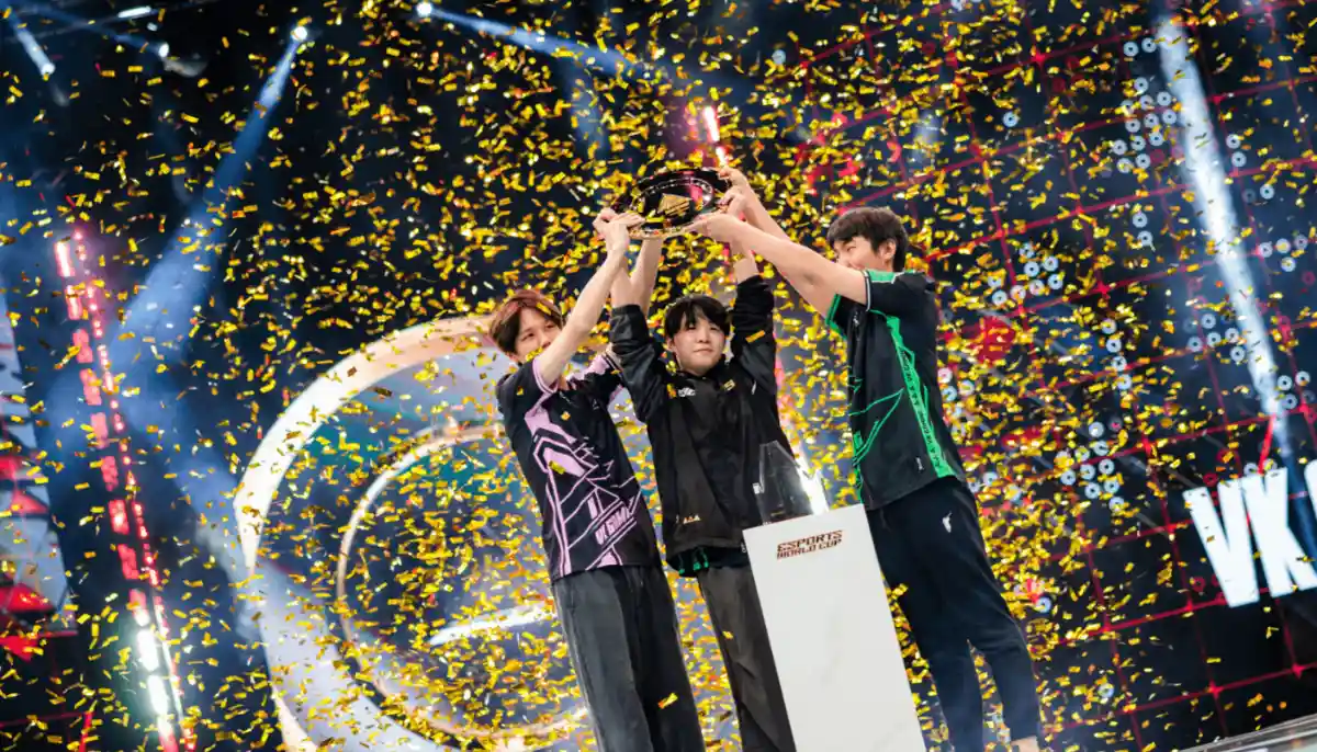 Tre e-sportspelare firar seger på scen och höjer en pokal medan konfetti regnar ner över dem.