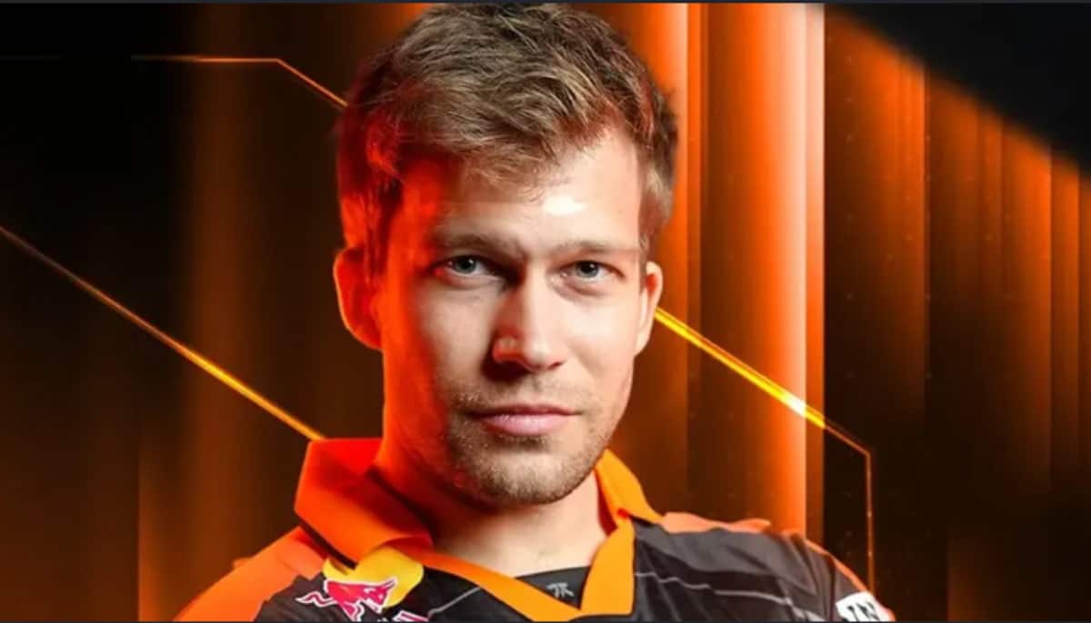 En e-sportspelare i en svart och orange tröja med Red Bull-logga mot en orange bakgrund.