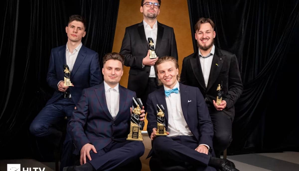 Fem män i kostym poserar med prispokaler framför svart och guld bakgrund.
