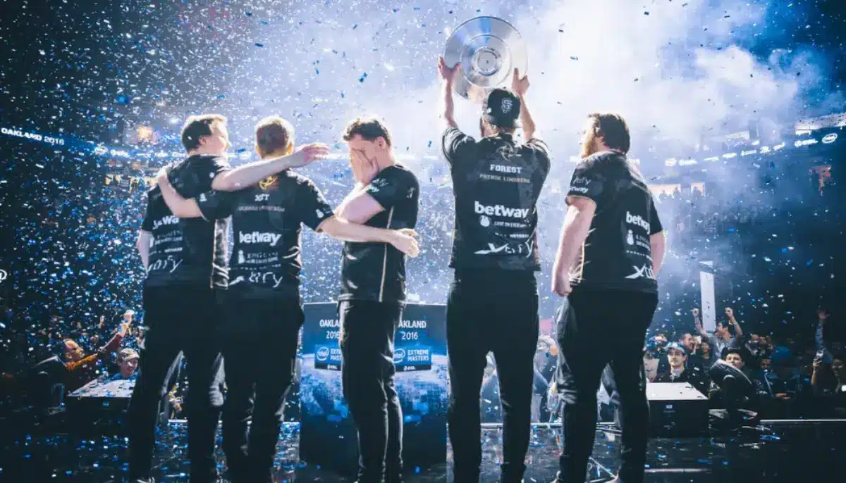 Ett e-sportlag firar seger på scen med pokal och konfetti inför jublande publik.