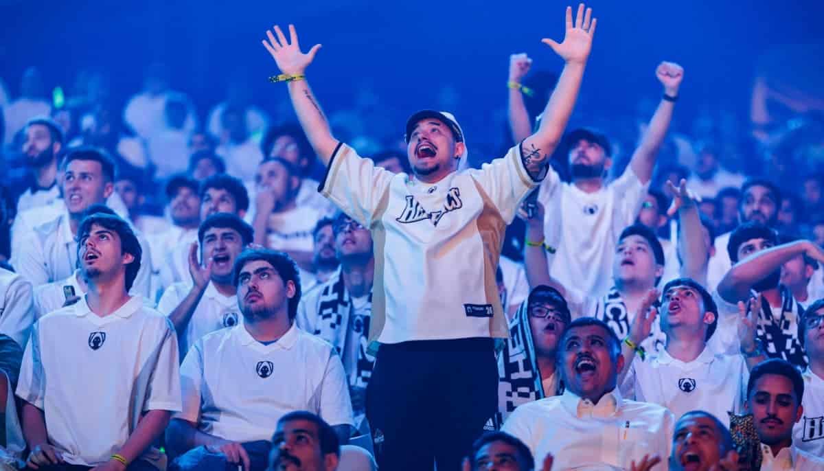 Publik i vitt firar med armarna i luften under en esportmatch, stämningen är entusiastisk och festlig.
