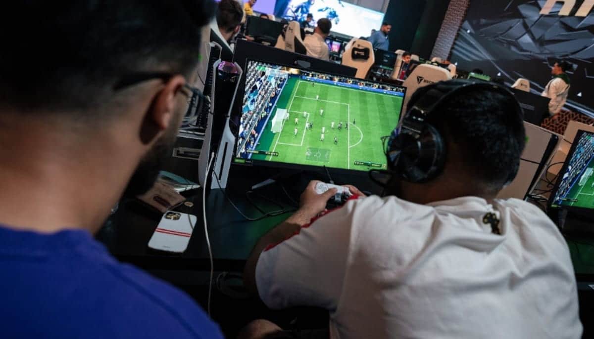Två personer spelar ett fotbollsspel på dator under en e-sportturnering, med åskådare runtomkring.