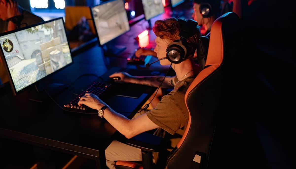 Ung man spelar datorspel på e-sportturnering, sitter i gamingstol med headset och tangentbord.