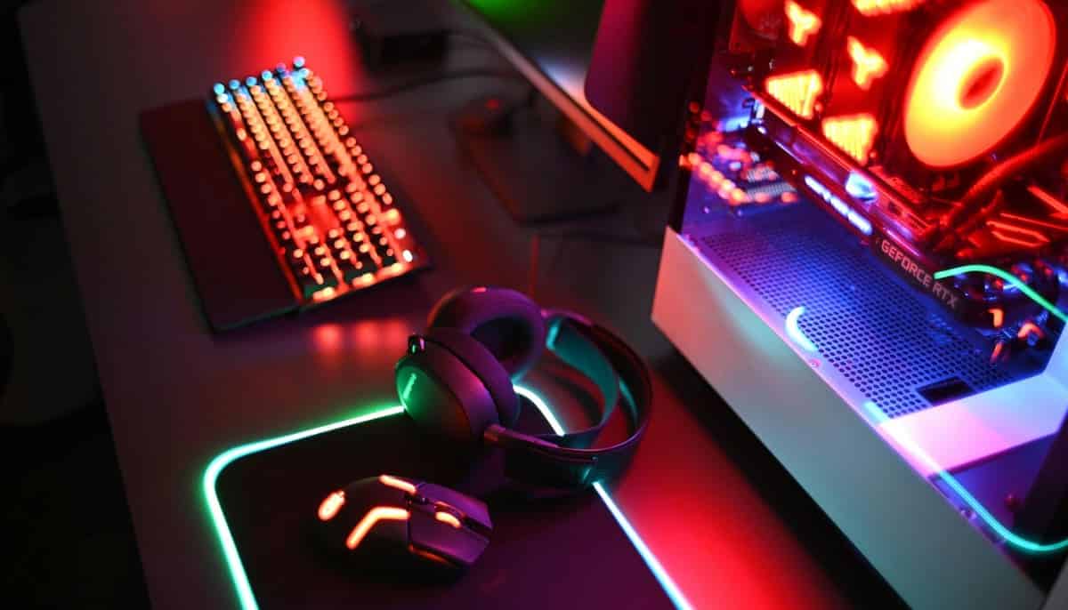 Gamingdator, tangentbord, mus och headset på skrivbord med färgglad led-belysning.