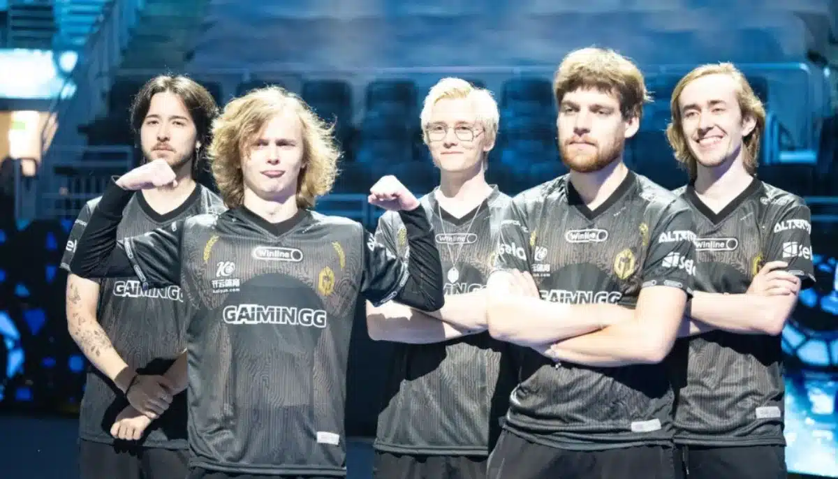 Fem e-sportspelare i Gaimin Gladiators-tröjor poserar på en arena med tomma läktare i bakgrunden.