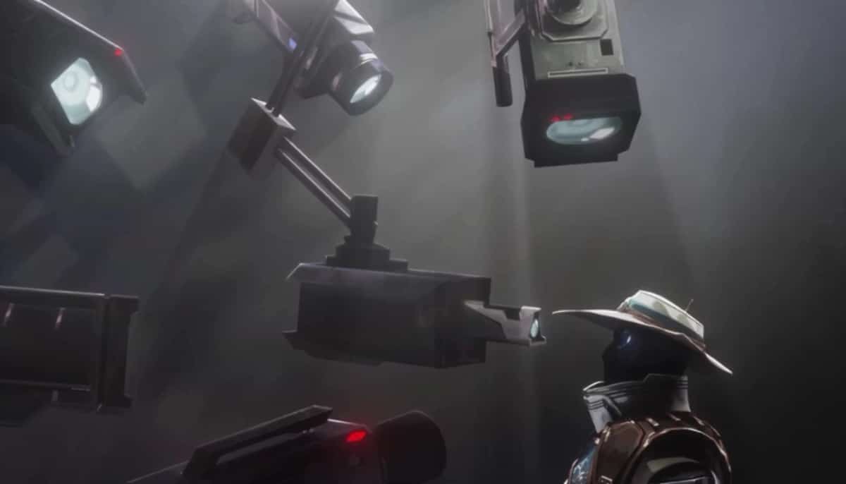 En robot med hatt står framför flera stora strålkastare och övervakningskameror i ett mörkt rum.