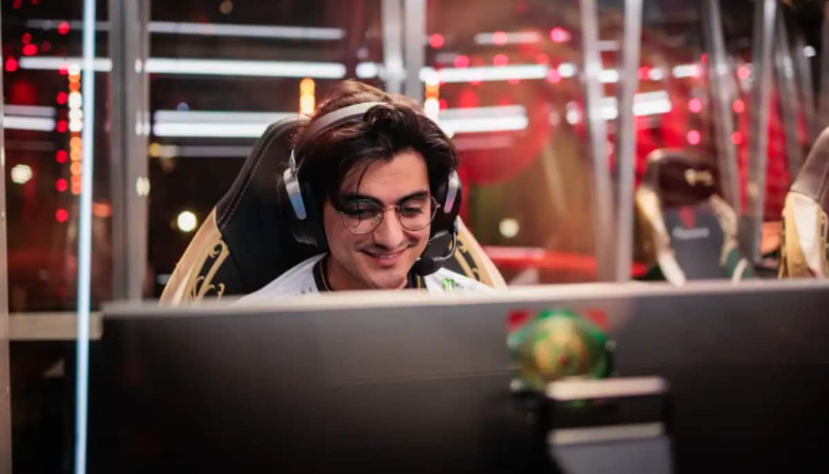 E-sportspelare med headset och glasögon ler medan han spelar framför en datorskärm.