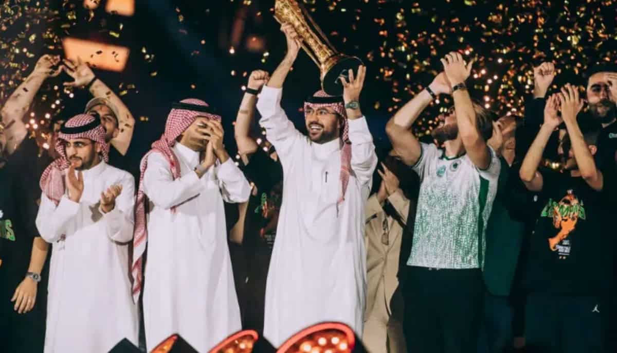 Personer firar på scen med en stor pokal, konfetti faller och stämningen är festlig.