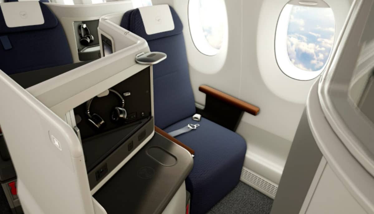 Flygplansstol i business class med fönsterutsikt, mörkblå klädsel och moderna detaljer.