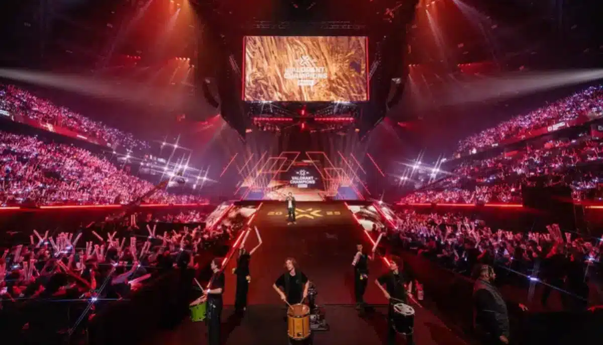 Fullsatt arena med ljusshow under Valorant Champions-evenemanget, med scen och trummisar i förgrunden.