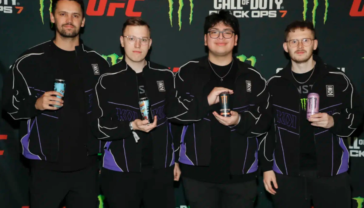 Ett lag e-sportspelare poserar på event med energidryck i händerna framför en sponsrad backdrop.