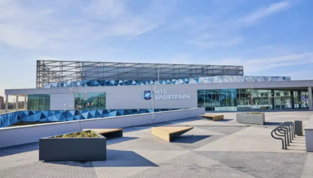 Modern arenaexteriör med MTK Sportpark-skylt, glasfasad och öppet torg med bänkar.