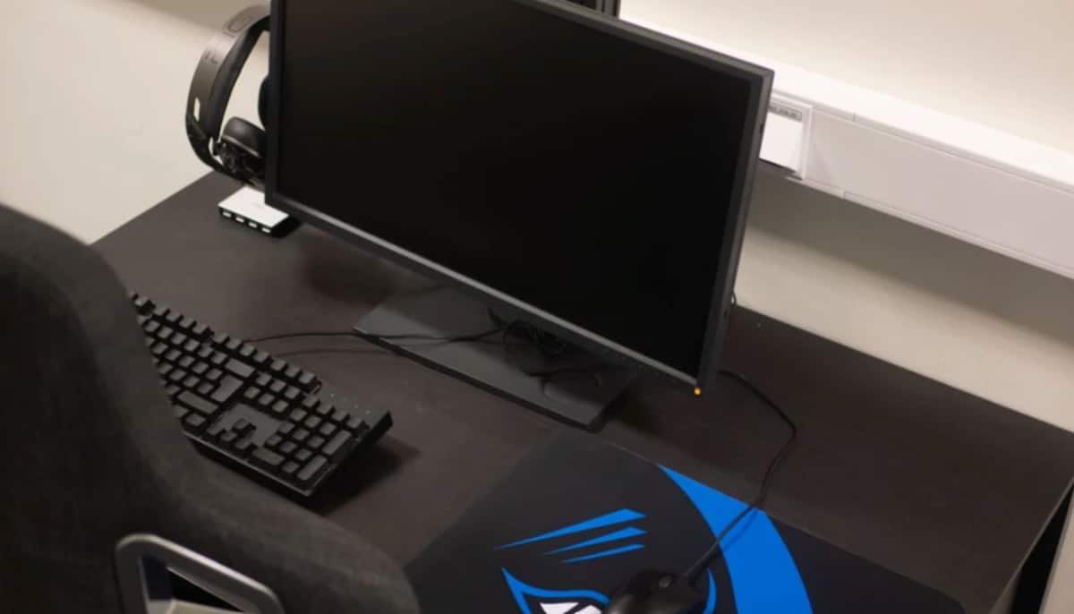 Datorsetup med skärm, tangentbord, mus och hörlurar på skrivbord i ett esport-rum.