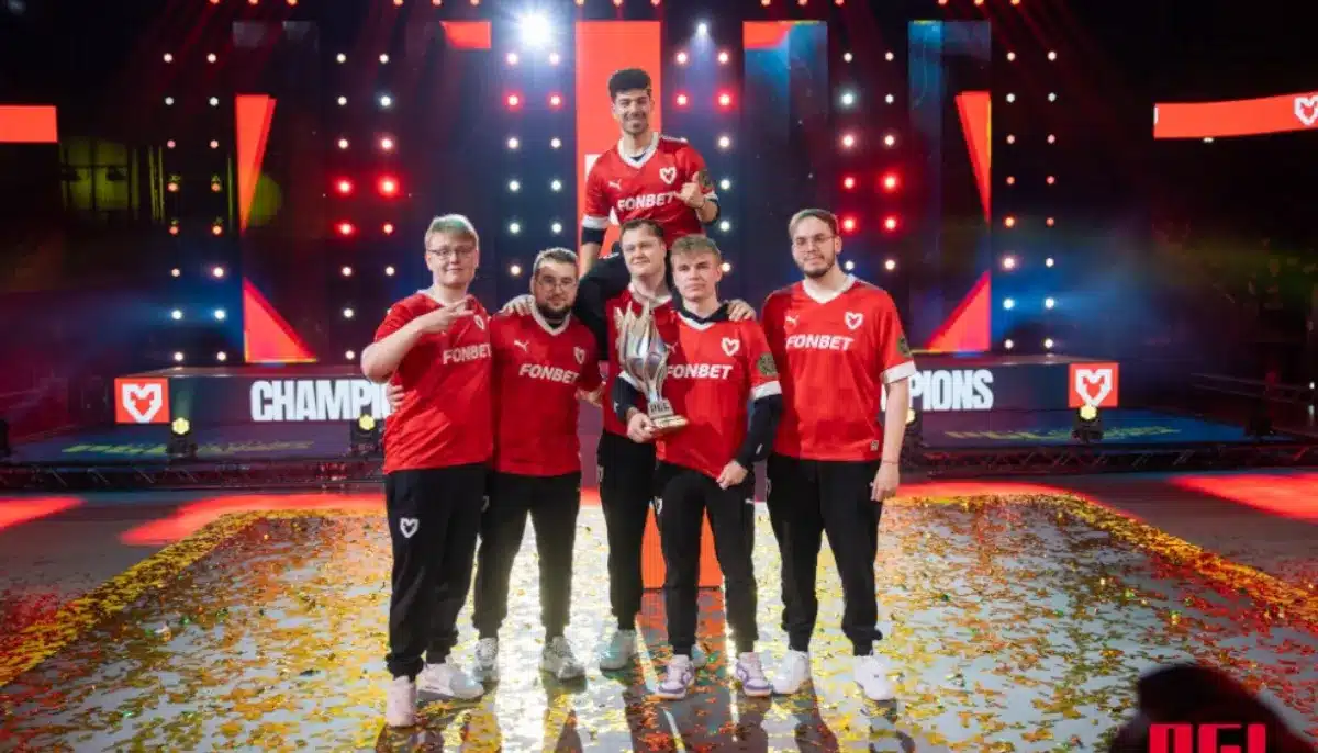 E-sportlag i röda tröjor firar seger på scen med pokal och konfetti under färgstarka ljus.