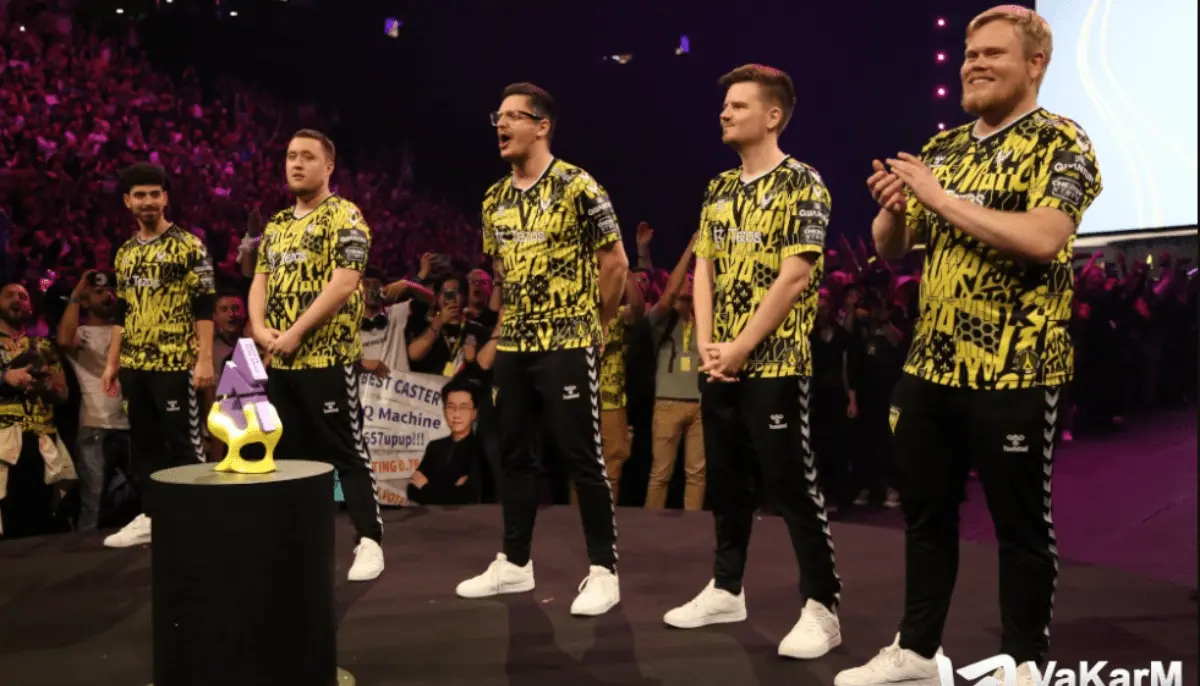 E-sportlag står på scen och applåderar bredvid pokal inför publik under turnering