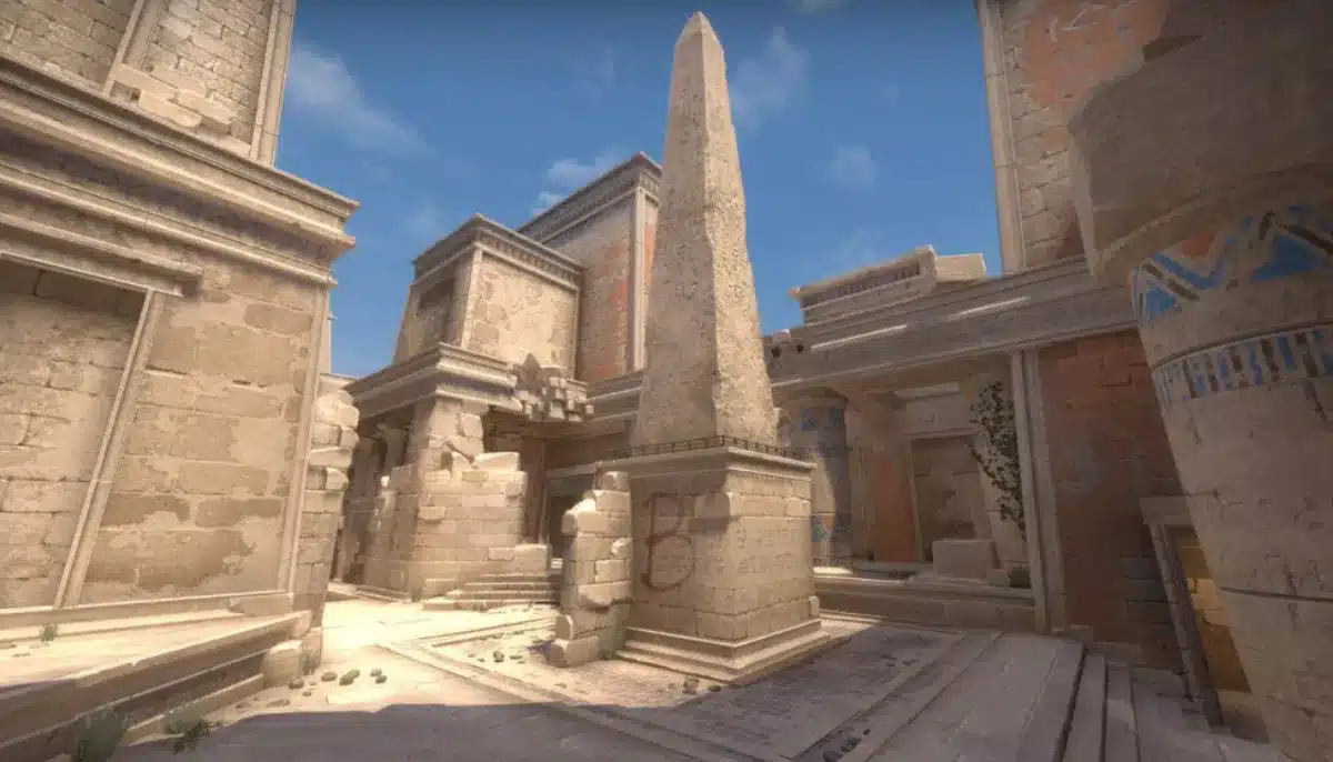 Spelmiljö från Counter-Strike 2 med sandfärgade ruiner och en hög obelisk i centrum på en tävlingskarta.