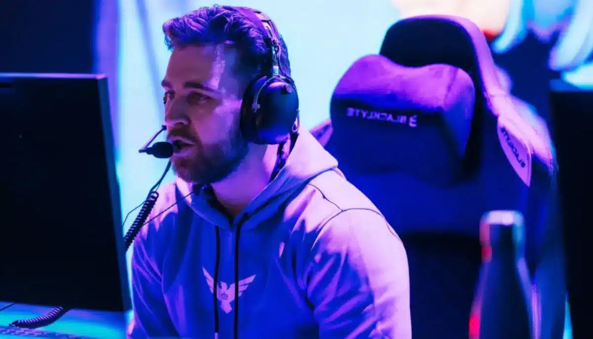 E-sportspelare med headset sitter vid dator på scen under tävling, upplyst av blå och lila ljus.