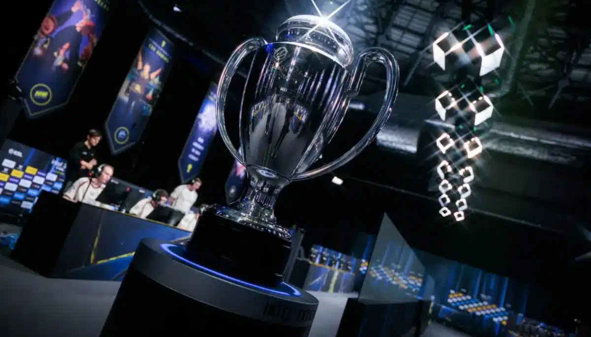 Pokal på scen under IEM-turnering, med spelare vid datorer och upplyst esportarena i bakgrunden.