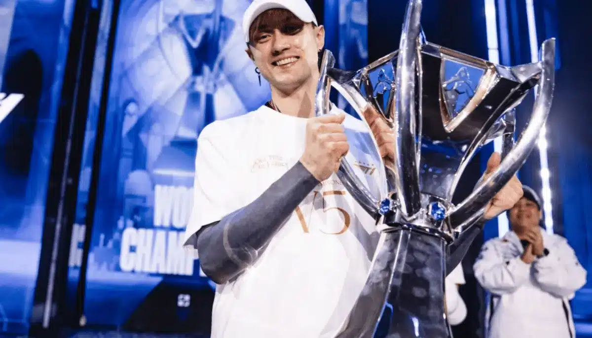 Rekkles ler och håller en stor pokal på scen efter turneringsseger, med jublande lagkamrater i bakgrunden