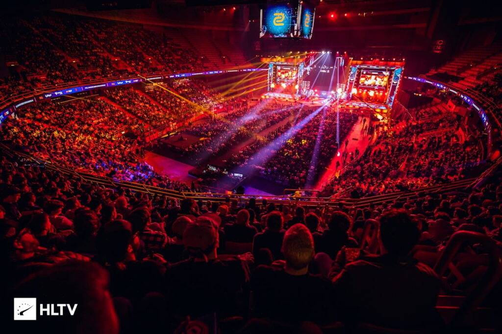A packed arena filled with spectators enjoying a vibrant esports event, illuminated by colorful stage lights and large screens.