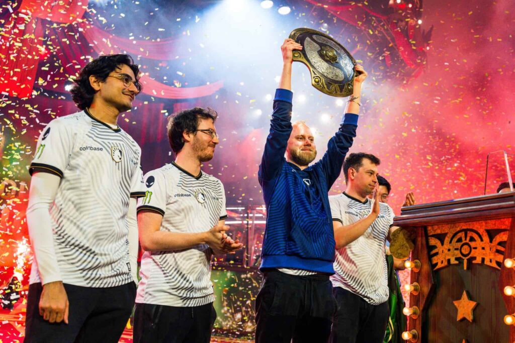 Team Liquid celebrating their victory at The International 2024 (TI13), with confetti falling on stage as a team member lifts the Aegis of Champions trophy, surrounded by teammates in white jerseys.