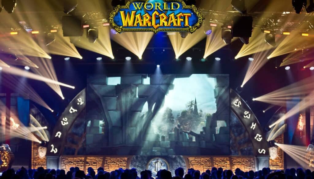 Stage set for a World of Warcraft event, featuring vibrant lights, a large screen displaying game imagery, and an engaged audience.
