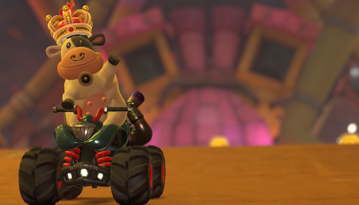 A cartoon cow wearing a golden crown and holding a drink rides a green ATV in a colorful, whimsical racing environment of Mario Kart World.