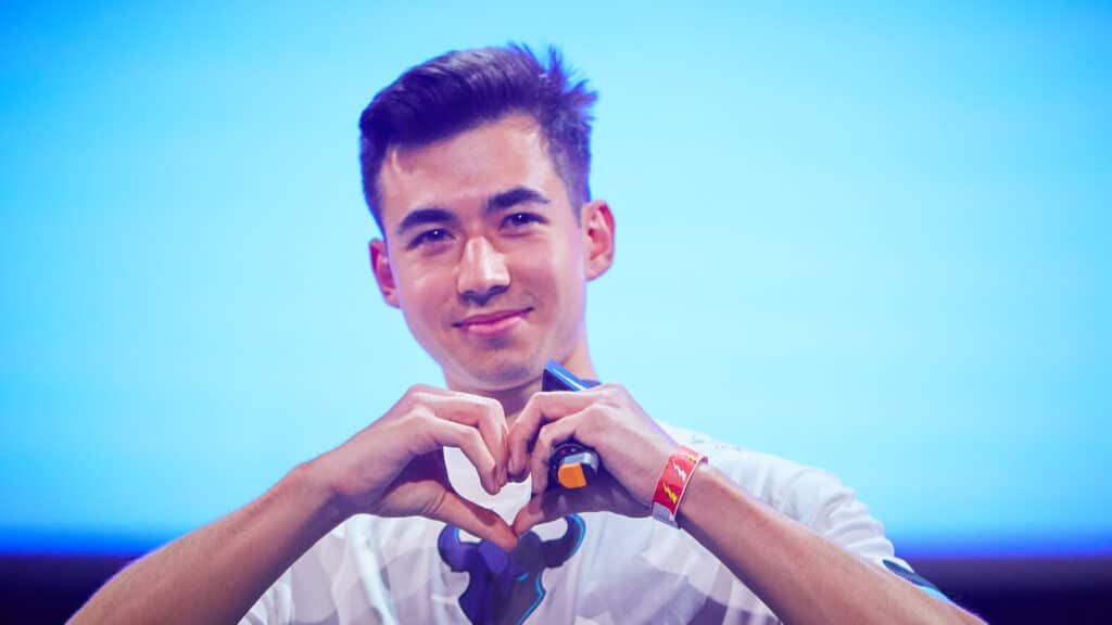 Image of Dillon 'Attach' Price making a heart sign with his hands on a light blue background