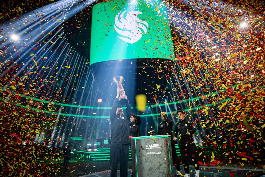 Image of Team Falcons celebrating victory at RLCS Raleigh Major. Red and yellow confetti falls from the ceiling and surrounds the players.