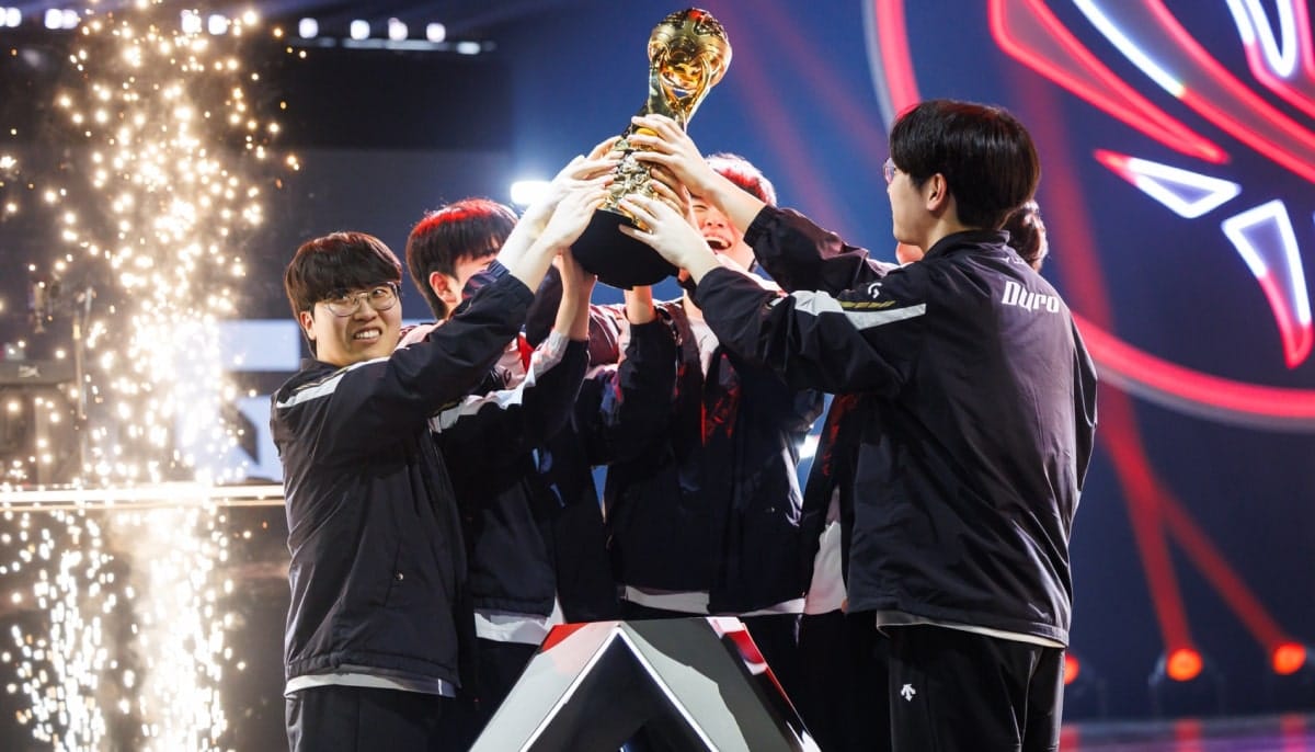 A team of five young men in matching jackets lift a golden trophy together on stage, surrounded by celebratory sparks and colorful lights, expressing joy and triumph