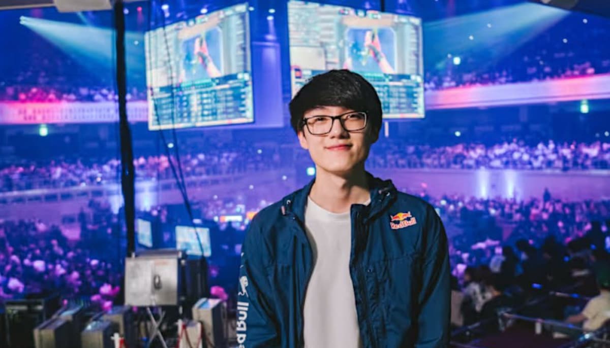 iiTz Timmy with glasses stands in a bustling esports arena. Large screens display game action above a crowd illuminated by vibrant purple and blue lights