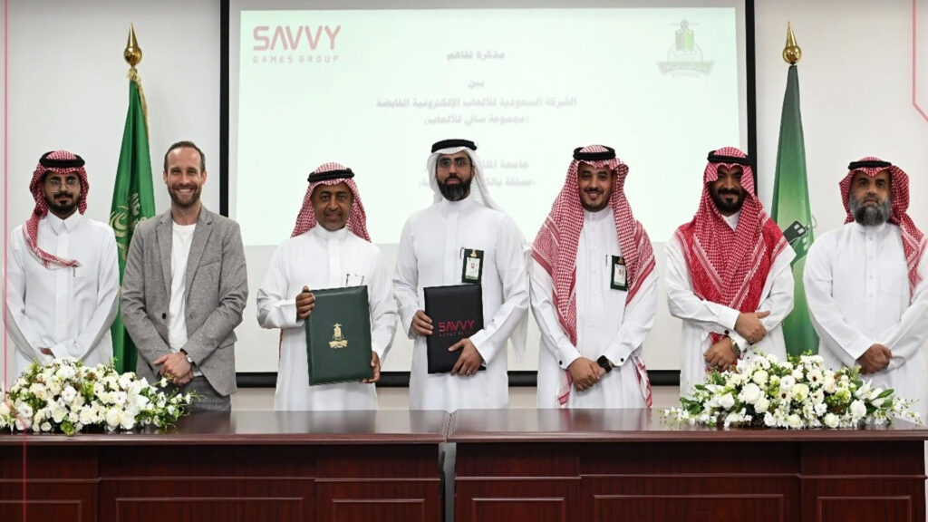 Image of Savvy Games Group and King Abdulaziz University members holding documents with each company's logo on the front