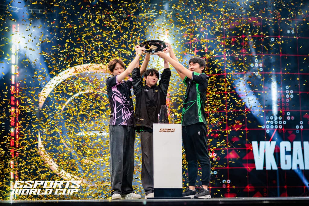 Image of VK Gaming Apex Legends players lifting trophy on Esports World Cup stage. Gold confetti is covering the players. The Esports World Cup logo is in the bottom left of the image