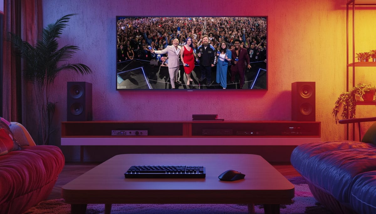 A cozy living room with a large TV displaying a group of people taking a selfie onstage with a cheering crowd