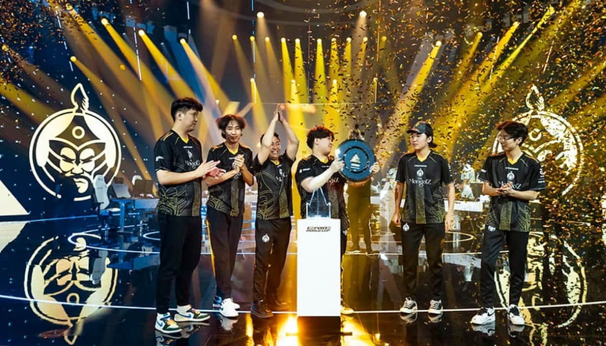 A victorious esports team celebrates on stage, holding a trophy amid golden confetti and bright spotlights