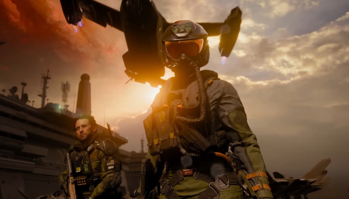 Two figures in military gear stand on an aircraft carrier deck at sunset