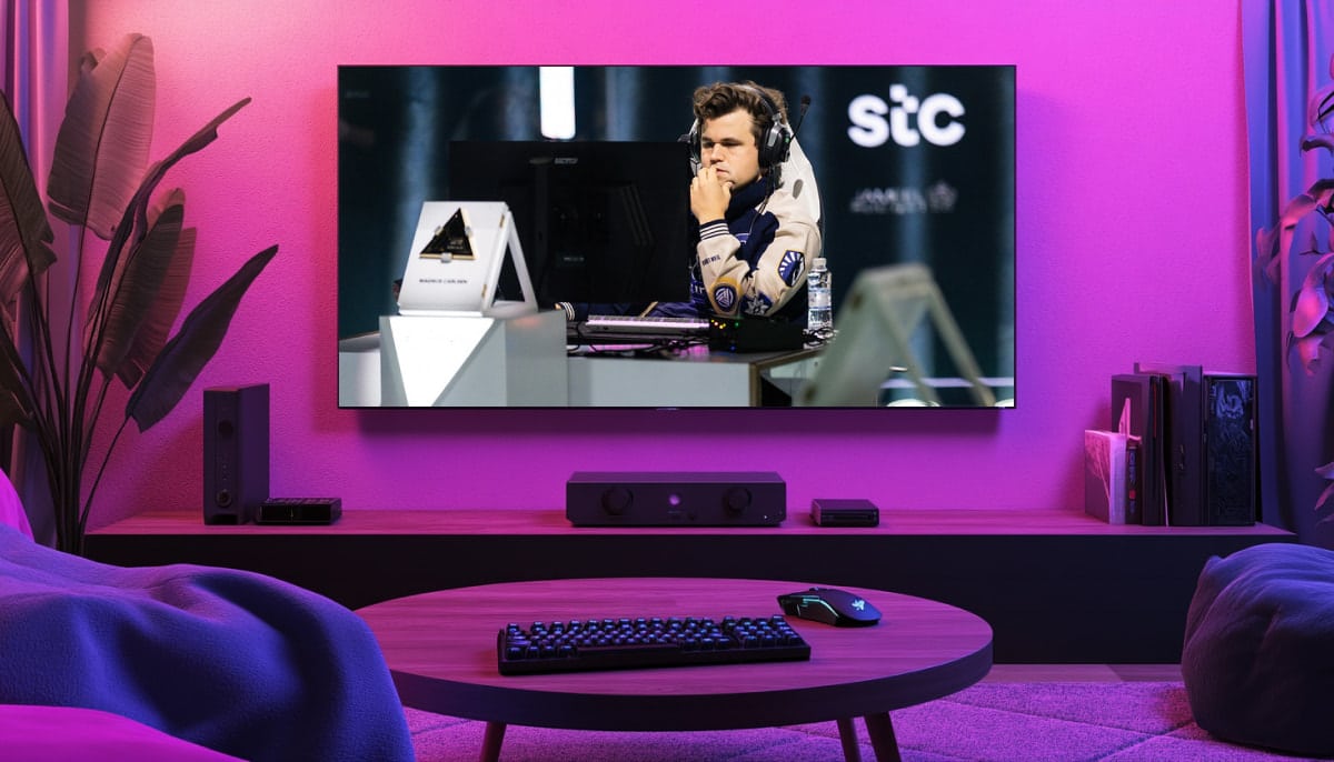 A living room with a large TV displaying a gaming event. A focused player with headphones is shown