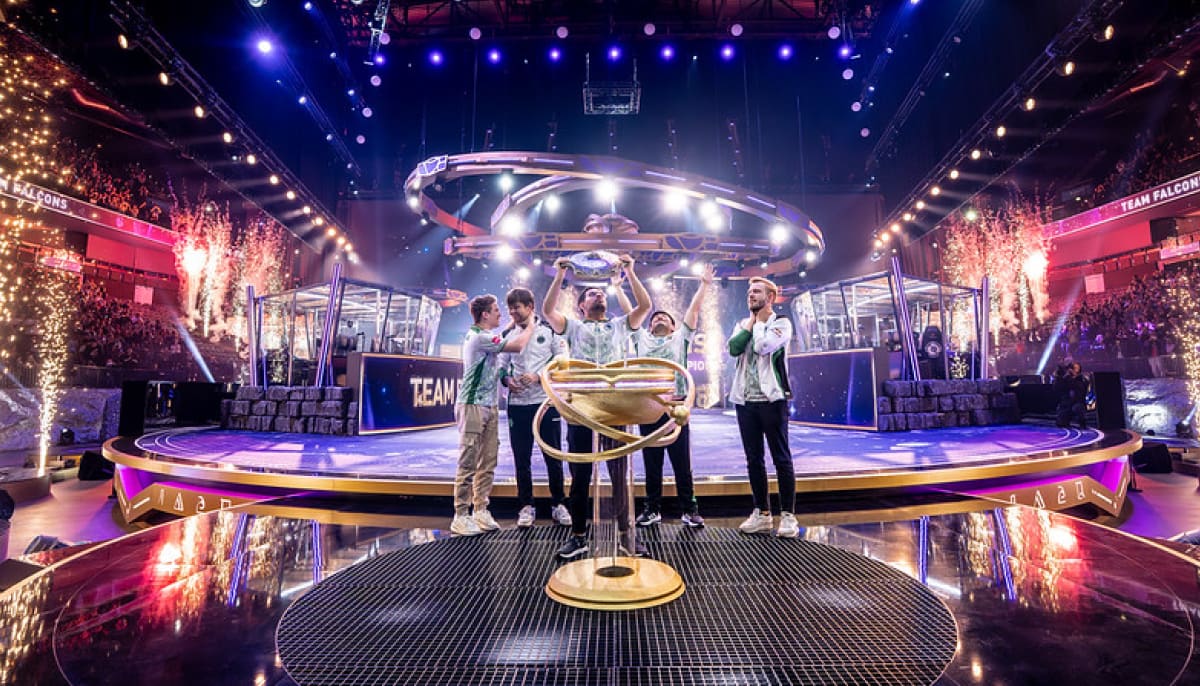 A victorious esports team celebrates on stage with a large trophy, surrounded by vibrant lights and fireworks, exuding excitement and triumph