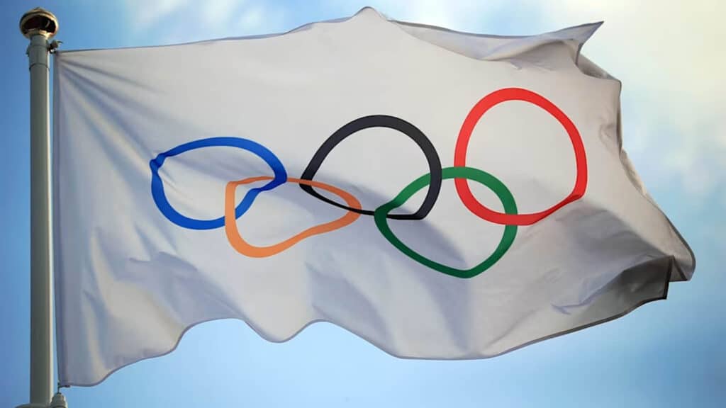 Image of Olympic flag flying in the wind. Blue sky with clouds are in the background