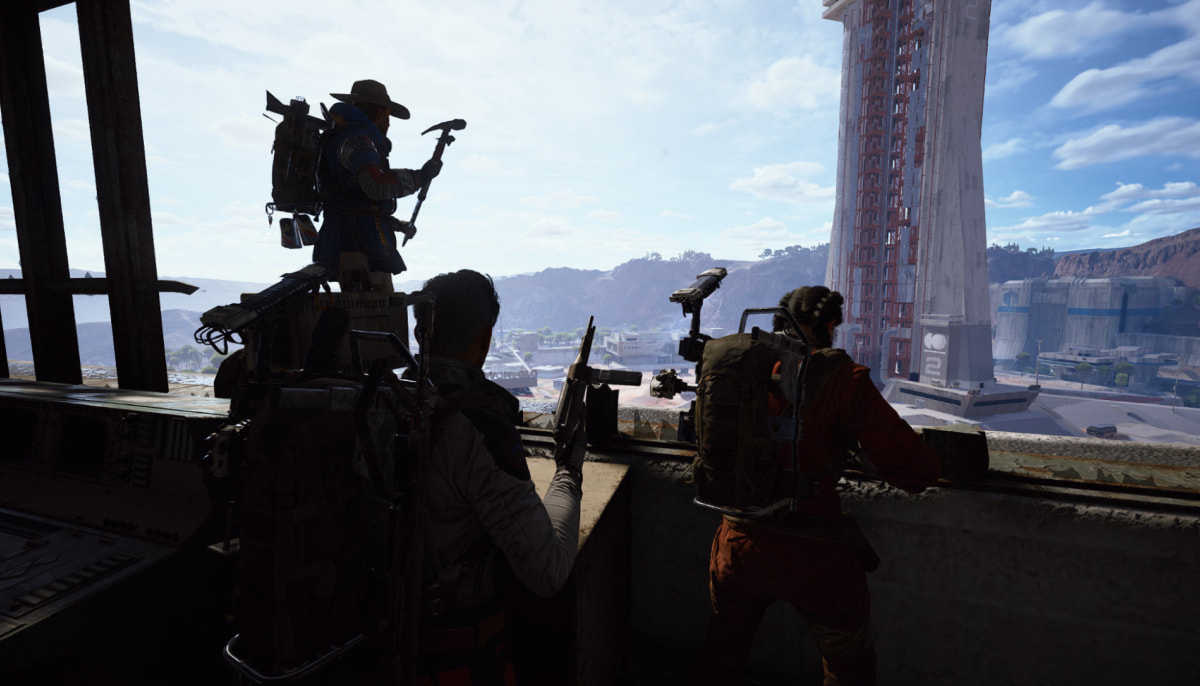 Three explorers, equipped with gear, look out from a control room towards a large rocket structure in Arc Raiders