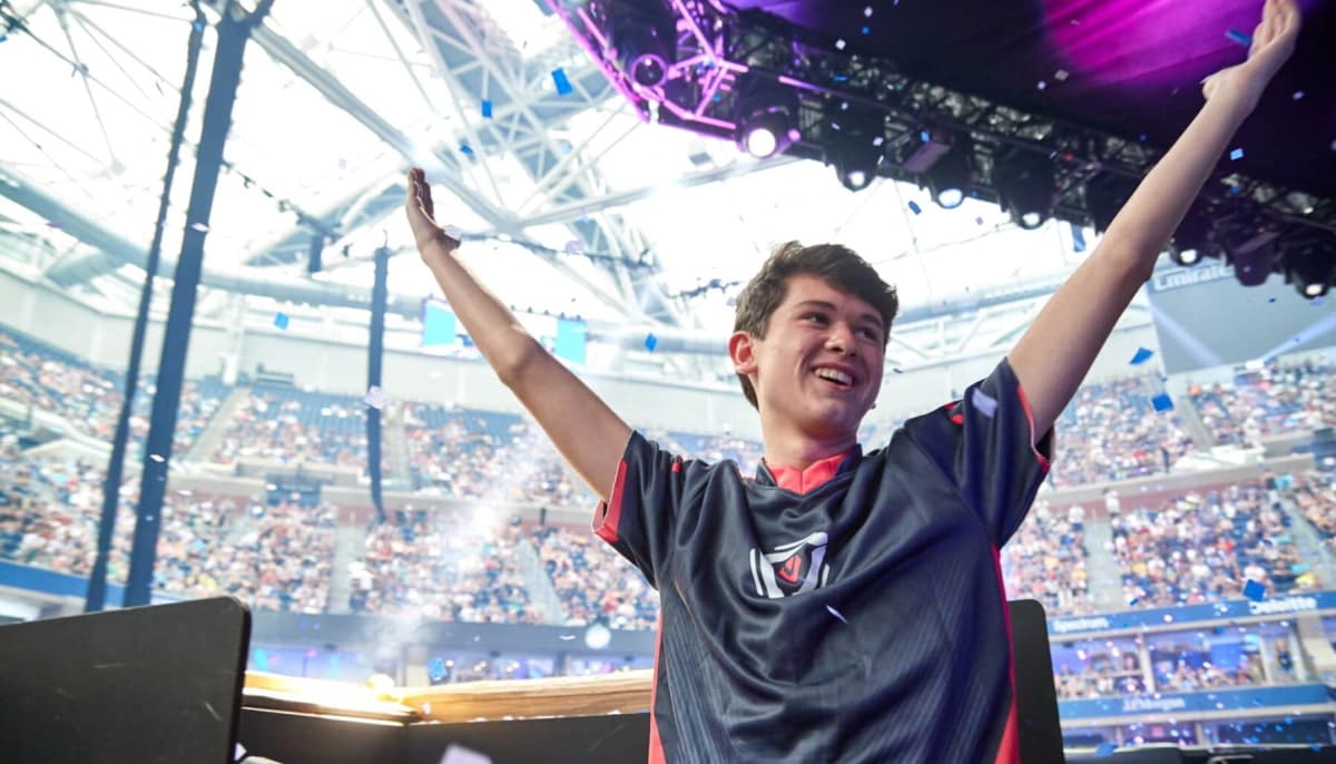 Bugha triumphantly raises their arms amidst confetti in a packed stadium