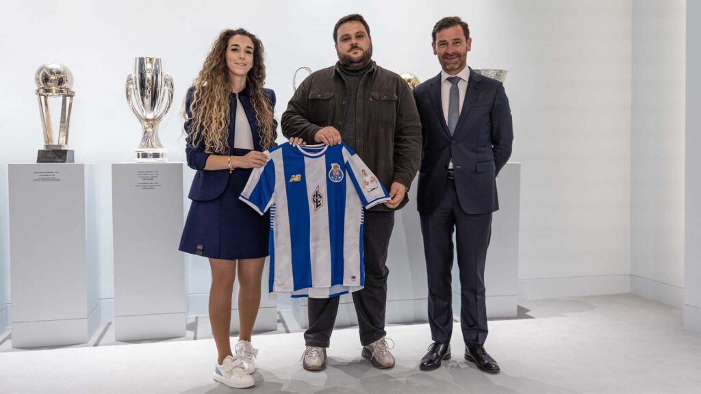 Image of FC Porto and Luna Esports representatives standing together while holding FC Porto jersey. A collection of football trophies on plinths are in the background