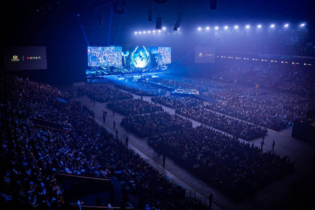 Image of Karmine Corp KCX community event stage illuminated by blue lights. A capacity crowd is sat in front of the stage