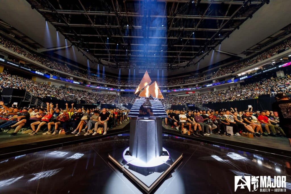 Image of BLAST.tv Austin Major 2025 trophy illuminated by white light and flames from stage. A capacity crowd is in the background